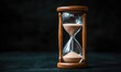 © NovaVision - Classic wooden hourglass with fine sand flowing against a dark background embodies the passage of time.