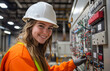 © designermetin - Smiling female electrical engineer wearing safety gear working on industrial control panel with colorful wiring