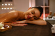 © Home-stock - Harmonious happy woman lying at spa salon table among aroma candles, waiting for therapist, body massage concept