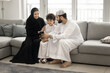 © fizkes - Smiling Arab family with little son using smartphone at home, watching videos, spend pastime on internet, enjoy digital communication or new mobile amusing application. Modern lifestyle, gadget usage