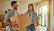 © remake - Happy couple carrying cardboard boxes during relocation to new apartment. Young adults in denim smiling at each other while moving into bright modern home with natural light and plants. Fresh start