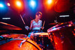 © Zamrznuti tonovi - Female drummer performing energetically on stage under colorful lights