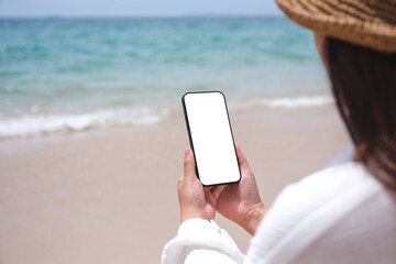 Wall Mural - mockup image of a woman holding mobile phone with blank desktop screen by the sea