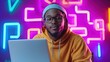 © Vilaysack - A person in a hoodie sits in front of a laptop, illuminated by vibrant neon lights.