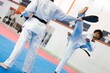 © Studio Marmellata - A martial artist in a white uniform and black belt extends a high leg kick toward a target pad held by a partner on a blue mat during intense indoor martial arts training