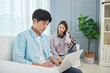 © Dialogue Frame - A young Asian man is using a laptop, while a woman with a headset around her neck is looking at him irritably.