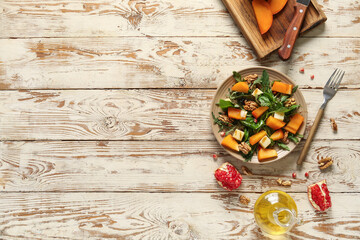 Wall Mural - plate of delicious salad with persimmon, walnut and pomegranate seeds on white wooden background
