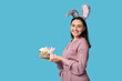 © Pixel-Shot - Happy young woman in bunny ears with sweet Easter cake and toy rabbit on blue background