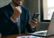 © ProArt Studios - Businessman Sitting with Laptop, Celebrating Victory on Smartphone