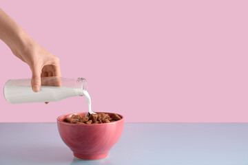 Wall Mural - young woman pouring milk into bowl with healthy cornflakes on color background