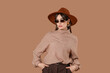 © Pixel-Shot - Beautiful young fashionable woman in hat and sunglasses on brown background