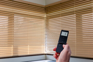 Leinwandbilder - Wooden blinds automated, beige color, on large corner windows. Mans hand holds black remote control panel for electric wood blinds, connected to smart home.