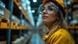© Prostock-studio - In a well organized logistics center, a woman with safety goggles and a helmet observes the automated processes. Rows of inventory surround her, showcasing efficient infrastructure.