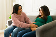 © AntonioDiaz - Happy pregnant woman feeling her baby kick while sitting on sofa and talking with doula during home visit