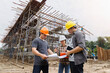 © skarie - Team of construction workers discussing project details with blueprint in construction site.
