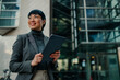 © Zamrznuti tonovi - Smiling businesswoman holding tablet and looking up in front of office building