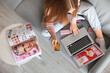 © Pixel-Shot - Woman with credit card and makeup products shopping online on sofa at home, top view