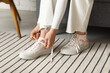 © Pixel-Shot - Young woman tying laces on stylish canvas sneakers, preparing for daily activities and casual outings