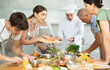 © JackF - Friendly smiling young woman talking to culinary enthusiasts during group cooking masterclass from professional chef..