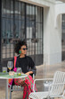© tessy morelli/Stocksy - Woman sitting at outdoor cafe with suitcase