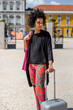 © tessy morelli/Stocksy - Fashionable tourist standing with suitcase Lisbon Cais do Sodre