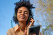 © tessy morelli/Stocksy - SMiling woman with phone outdoor listening music