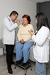 © Arlette - 80-year-old woman has her eyes, ears, and throat examined by a dark-skinned Latino doctor and his intern in the office as a checkup