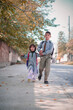 © Husnain - Elder brother holding hand of younger sister, in school uniform and backpacks, children walking to school.