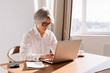 © Viktor Solomin/Stocksy - Senior woman working on laptop in bright office space