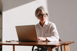 © Viktor Solomin/Stocksy - Older adult working on laptop at a desk in a well-lit indoor office