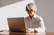 © Viktor Solomin/Stocksy - Mature professional woman working on laptop in a sunlit office