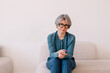 © Viktor Solomin/Stocksy - Stylish woman with gray hair seated on a light-colored couch