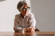 © Viktor Solomin/Stocksy - Thoughtful woman with silver hair and glasses posing in office