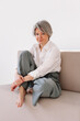 © Viktor Solomin/Stocksy - A woman with short gray hair sits on a light-colored couch