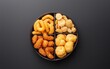 © creatfive - Overhead shot of four types of assorted fried snacks in a divided dark brown round bowl on a dark gray background. The snacks are golden brown and appear sweet and crunchy