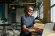 © BONNINSTUDIO/Stocksy - Smiling woman working on laptop in modern coworking