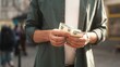 © VAKSMANV - Close-up view of young caucasian male holding and counting euro bills standing outside on crowded street. Stylish adult man looking at money after cashing out in ATM terminal.