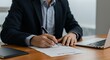 © addigital - Man Signing a Legal Document on Wooden Desk with Laptop Nearby