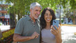 © Krakenimages.com - Middle-aged couple smiling at smartphone in sunny urban park, highlighting love and togetherness in outdoor city setting with vibrant nature background.