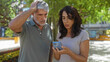 © Krakenimages.com - Middle aged couple looks concerned while viewing smartphone outdoors in urban park setting, capturing a candid moment of engagement and connection in city life