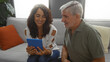 © Krakenimages.com - Middle-aged couple sitting on sofa, smiling at tablet in cozy living room, showcasing a warm, intimate indoor setting with a man and woman enjoying quality time together.