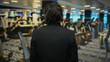 © Krakenimages.com - Man in a black suit standing indoors in a gym facing exercise equipment with blurred background, creating a modern and focused atmosphere.