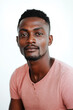 © Wilker - A close-up portrait of a young Black man against a plain, off-white background. The image is sharply focused on the subject's face, showing subtle details of his skin tone and facial hair. He sports