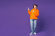 © ViDi Studio - Full body young smiling cheerful fun cool happy woman wear orange hoody casual clothes point index finger aside on area mockup isolated on plain purple background studio portrait. Lifestyle concept.