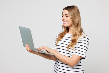 Young smart smiling happy IT woman wear striped t-shirt casual clothes hold use work on laptop pc computer chatting online isolated on plain solid white background studio portrait. Lifestyle concept.