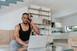 © .shock - African American man in glasses sitting at a table in a modern living room, using a laptop for business video chat, conversation with friends and entertainment