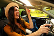 © Home-stock - Joyful lady enjoying listening to music while driving car and singing songs, woman ready for trip, backpack nearby on passenger seat