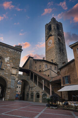 Wall Mural - The Torre Civica stands tall in Bergamo's old town square, surrounded by stone buildings, arched windows, and a brick paved plaza under a vibrant evening sky.