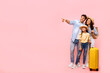 © Home-stock - Family travel concept. Happy parents with daughter carrying suitcase and pointing aside at empty space for advertisement, pink background