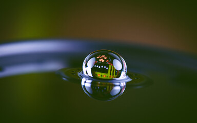 Poster - A macro shot captures a single water droplet resting on a surface, reflecting vibrant electronic components within its sphere against a blurred dark backdrop.